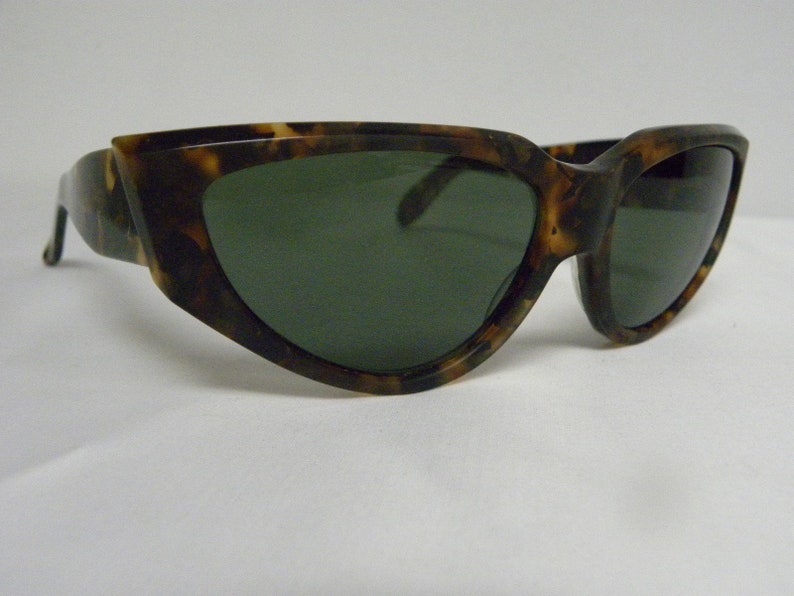 K&ouml;nnte beinhalten: Schildpatt-Sonnenbrille mit gr&uuml;nen Gl&auml;sern. Die Sonnenbrille hat eine einzigartige, eckige Form.