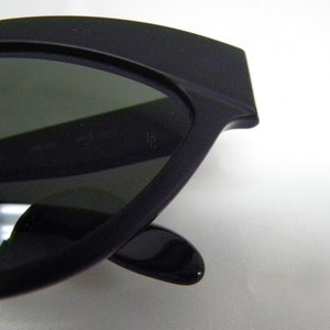 Puede incluir: Gafas de sol negras de ojo de gato con lentes grises oscuros. Las gafas tienen un marco negro grueso.
