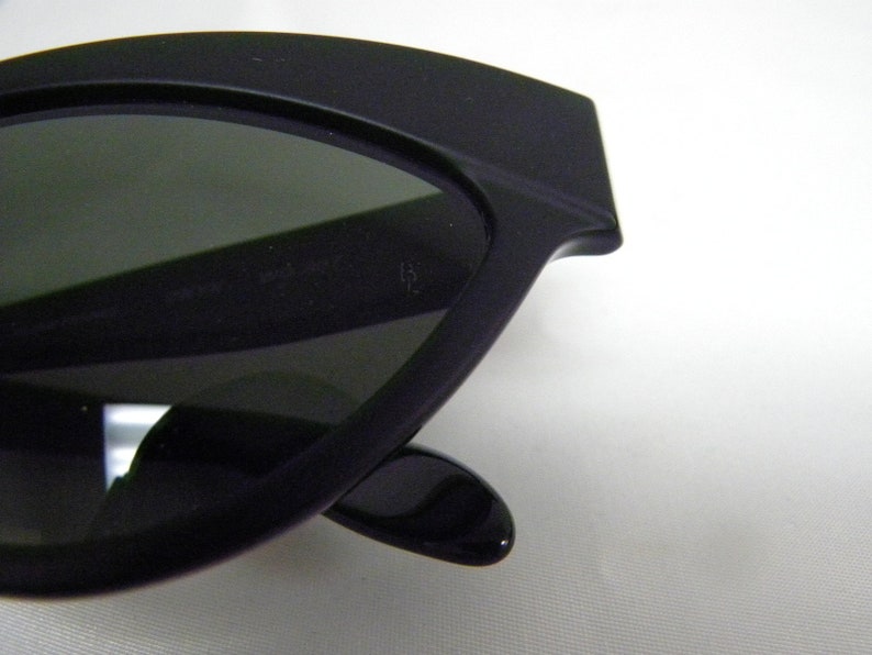 Puede incluir: Gafas de sol negras de ojo de gato con lentes grises oscuros. Las gafas tienen un marco negro grueso.