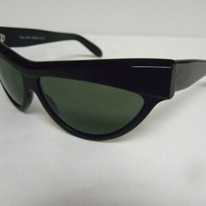 Puede incluir: Gafas de sol negras con montura estrecha y curvada y lentes verdes.