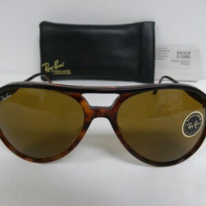 Puede incluir: Gafas de sol aviador de carey marr&oacute;n con lentes marrones. Las gafas tienen una barra de metal sobre el puente de la nariz y un logotipo de Ray-Ban en la lente derecha.