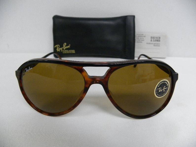Puede incluir: Gafas de sol aviador de carey marr&oacute;n con lentes marrones. Las gafas tienen una barra de metal sobre el puente de la nariz y un logotipo de Ray-Ban en la lente derecha.