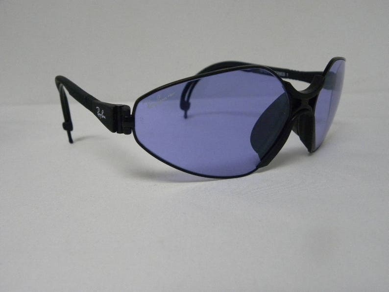 May include: Black wraparound sunglasses with a blue lens. The sunglasses have a flexible frame and a thin strap.