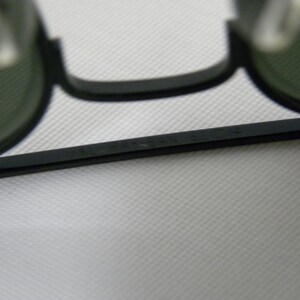 May include: Close-up of the black frame of a pair of round sunglasses with green lenses. The frame has the text "MADE IN ITALY" printed on it.