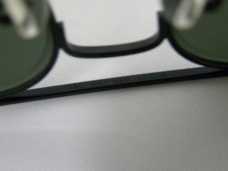 May include: Close-up of the black frame of a pair of round sunglasses with green lenses. The frame has the text "MADE IN ITALY" printed on it.