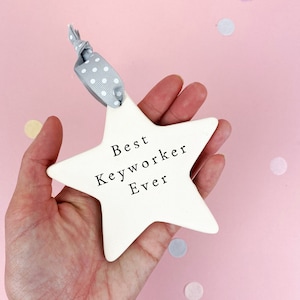 May include: White ceramic star ornament with a gray ribbon and white polka dots. The star has the text "Best Keyworker Ever" written on it.