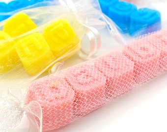 May include: Three small bags filled with colorful letter shaped wax melts. The bags are made of sheer white mesh and tied with white ribbon. The wax melts are in the colors pink, yellow, and blue.