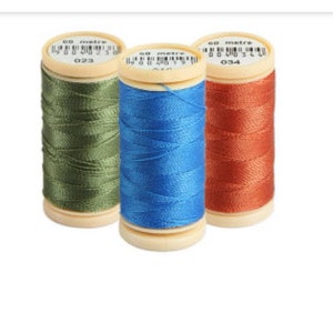 Op de afbeelding: Drie spoelen garen, een groene, een blauwe en een oranje. Elke spoel is gemarkeerd met "60 meter" en heeft een nummer. De spoelen bevinden zich op een witte achtergrond.