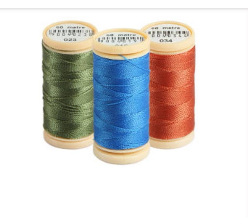 Op de afbeelding: Drie spoelen garen, een groene, een blauwe en een oranje. Elke spoel is gemarkeerd met "60 meter" en heeft een nummer. De spoelen bevinden zich op een witte achtergrond.