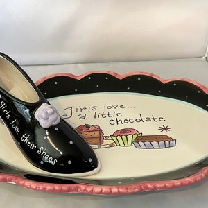May include: A black and white oval serving dish with a pink scalloped edge. The dish has a black high-heeled shoe with white polka dots and the text "Girls love their shoes" on the side. The dish also has the text "Girls love... a little chocolate" and a drawing of chocolate desserts.