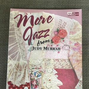 May include: Book cover with the title "More Jazz from Judy Murrah" and the subtitle "New Shapes & Great Ideas for Wonderful Wearable Art". The cover features a pink background with lace, fabric, and floral designs.