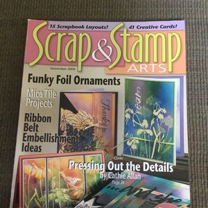May include: A magazine cover for Scrap & Stamp Arts, November 2004 issue. Features include "Funky Foil Ornaments," "Mica Tile Projects," and "Ribbon Belt Embellishment Ideas." The cover art showcases colorful scrapbook and card designs, with the text "Pressing Out the Details."