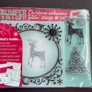 May include: A Christmas embossing kit in a clear plastic package. The kit includes a snowflake embossing folder, three stamps, four designer papers, glitter paper, and foiled paper. The package has text that reads "BUMPER 3-IN-1 GIFT!"