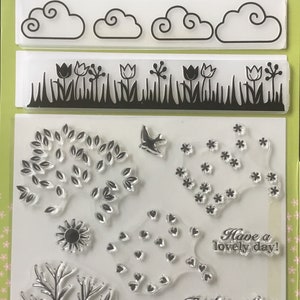 May include: A set of clear stamps for cardmaking featuring a variety of images including trees, flowers, clouds, a bird, a sun, hearts, and a bunny. The stamps are arranged on a white background with green borders and the text "For all seasons Build-a-scene stamp and embossing set" at the top. The text "Have a lovely day! Thinking of you Sending you sunshine With love Thankful FOR YOU" is also included on the sheet.