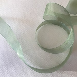 May include: A pale green sheer ribbon with a satin finish. The ribbon is curled and twisted on a white background.