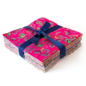 May include: A stack of pink fabric squares with a paisley pattern, tied together with a navy blue ribbon.