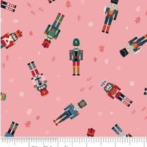 May include: A pink fabric featuring a repeating pattern of nutcracker figures in various uniforms, interspersed with small white snowflakes and light pink tree silhouettes. A white ruler at the bottom shows 5 inches of length.