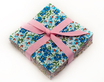 May include: A stack of fabric squares with a floral print in shades of blue, white, and green. The squares are tied together with a pink ribbon.