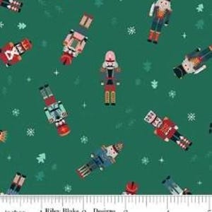 May include: A dark green fabric featuring a repeating pattern of nutcracker figures in various colors including red, blue, and pink, interspersed with white snowflakes and small tree shapes, with a ruler showing inches at the bottom edge.