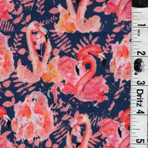 May include: A fabric with a repeating pattern of pink flamingos and floral elements on a dark blue background. The flamingos have black beaks and are surrounded by pink and orange watercolor-style flowers and leaves. The ruler shows measurements in inches.