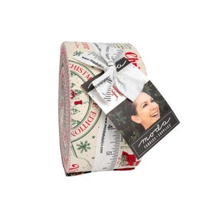 May include: A rolled fabric bundle featuring a Christmas-themed design with red and green accents on a cream background. The fabric is tied with a white ribbon and a tag with a woman's image and the words "moda FABRICS + SUPPLIES".