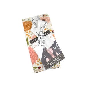 May include: A stack of folded fabric featuring a floral pattern with orange, pink, and yellow flowers and small ladybugs on a cream background. The fabric is tied with a white ribbon printed with a ruler design and a tag labeled Moda Fabrics Supplies.