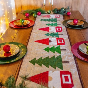 May include: A festive Christmas table setting with a quilted table runner featuring red and green Christmas trees and Santa Claus designs. The table is set with red and green plates, gold chargers, and ornaments.