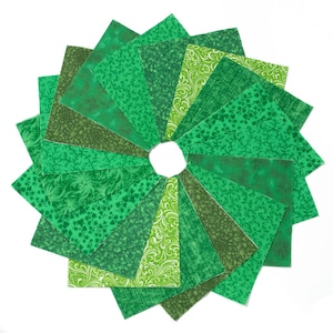 May include: A circular arrangement of green fabric squares in various shades and patterns, including floral and textured designs. The squares are arranged around a central white circle, creating a fan-like appearance. The fabrics are in shades of light, medium, and dark green.