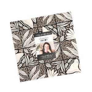 May include: A square stack of fabric squares featuring a repeating botanical pattern in black, white, and taupe. A rectangular paper label is attached to the center, displaying the text "moda IMPRINT" and a photograph of a person smiling.