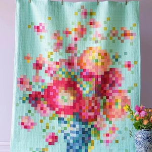 May include: A large, light blue floral quilt with a pixelated design. The quilt features a vibrant bouquet of flowers in shades of pink, red, orange, and yellow, arranged in a blue vase. The quilt is hanging from wooden clips.