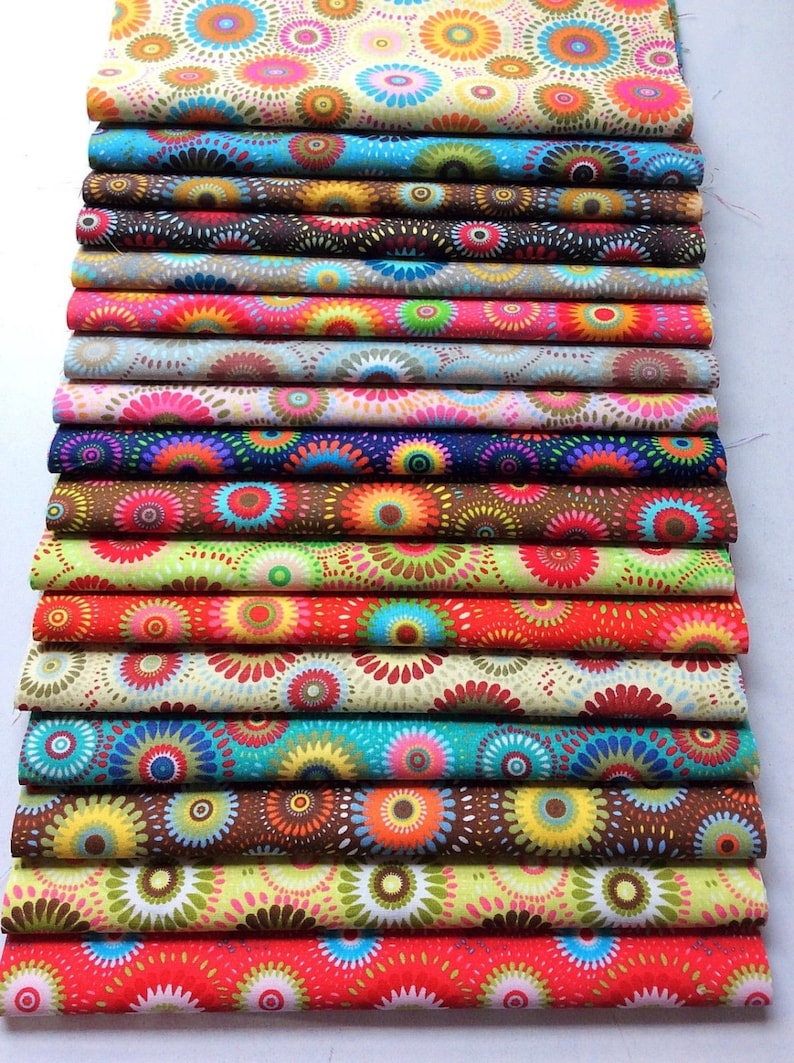 May include: A stack of colorful fabric featuring a repeating pattern of concentric circles in various shades of red, orange, yellow, green, blue, and purple. The fabric is arranged in a stack, with each layer slightly offset from the one below it.