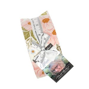 May include: A stack of fabric squares featuring a floral pattern in shades of pink, green, and blue, tied with a white ribbon printed with a ruler design. A tag attached to the ribbon displays the text Moda Fabrics and Supplies and Wildberry.