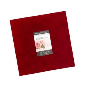 May include: A square piece of deep red fabric with pinked edges. A rectangular paper label is attached to the center, featuring the text "moda", "3 Sisters Solids", and "moda FABRICS+SUPPLIES" alongside an illustration of two pink roses.