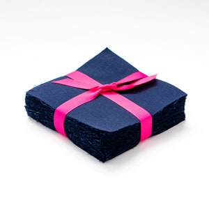 May include: A stack of navy blue fabric squares tied with a bright pink ribbon. The fabric appears to be a textured material, and the ribbon is wrapped around the stack in a bow.