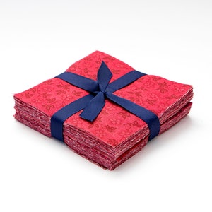 May include: A stack of red fabric squares with a floral pattern, tied together with a navy blue ribbon.