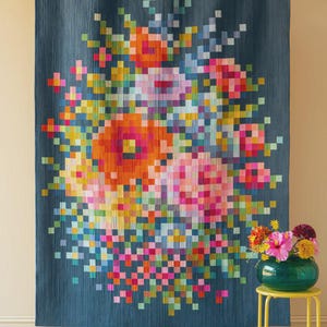 May include: A large, pixelated floral tapestry in shades of orange, pink, and blue hangs against a neutral wall. The artwork features a bouquet of flowers with a variety of colors. A small yellow side table holds a vase of flowers.