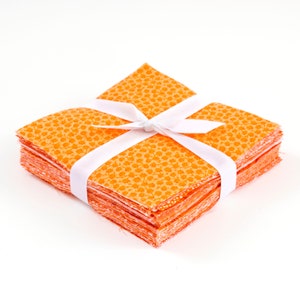May include: A stack of orange fabric squares with a white floral pattern, tied together with a white ribbon.