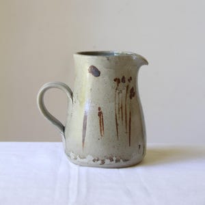 May include: A light grey ceramic jug with a brown handle and brown abstract designs.