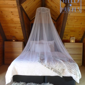 May include: A white canopy mosquito net hangs over a white bed with a gray throw blanket in a wooden cabin with a wood paneled ceiling. The text "STELLA MURALS" is visible in the upper right corner of the image.