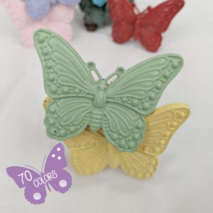 May include: A stack of three butterfly-shaped decorations in shades of green and yellow. The top butterfly is a light green, the middle one is yellow, and the bottom one is partially visible. Other butterfly decorations in pink and red are in the background. The image includes text that says "70 colors".