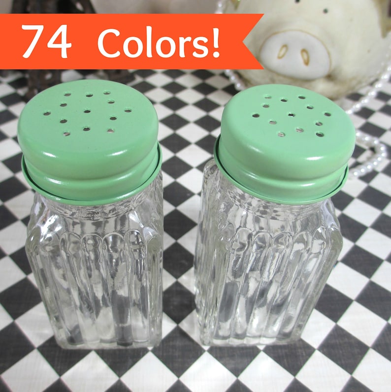 May include: Two clear glass salt and pepper shakers with light green metal lids. The shakers have a square, ribbed design. The text "74 Colors!" is in an orange banner above the shakers.