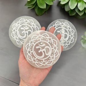 May include: Three white selenite crystal discs with an etched Om symbol and mandala design.