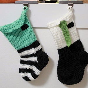 May include: Two crocheted Christmas stockings hanging on hooks. One stocking is green and white striped with a black bow. The other stocking is white with a green tie and black cuff.