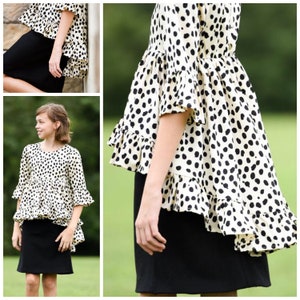 May include: A cream-colored top with a black dalmatian-style spot pattern, featuring three-quarter length sleeves with ruffled cuffs and a high-low hemline with a ruffled edge, paired with a solid black knee-length skirt.