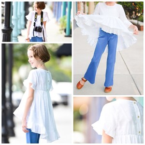 May include: A white, short-sleeved dress with a ruffled hem and small, gold-colored buttons down the back. The dress is paired with blue pants and brown sandals. A black camera with a white strap is also visible.