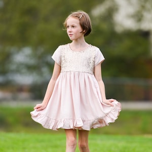 May include: A light pink dress featuring a sequined bodice with short sleeves and a gathered skirt with a ruffled hemline. The dress has a round neckline and a soft, flowing silhouette that falls above the knee.