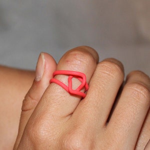 Puede incluir: Primer plano de una mano con un anillo de color rosa brillante. El anillo est&aacute; hecho de un material flexible y tiene un dise&ntilde;o geom&eacute;trico.