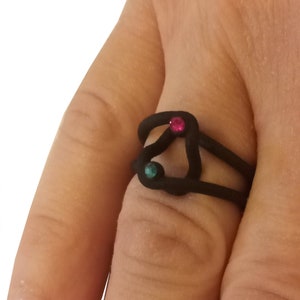以下が含まれることがあります： ピンクとターコイズの小さな宝石が2つ付いた黒いリング
