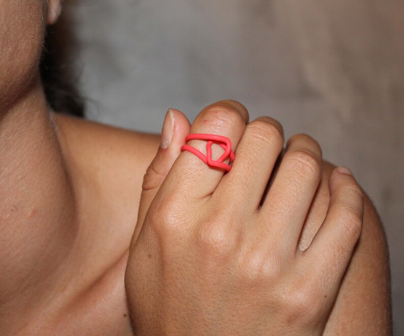 Puede incluir: Primer plano de una mano con un anillo de color rosa brillante. El anillo est&aacute; hecho de un material flexible y tiene un dise&ntilde;o geom&eacute;trico.