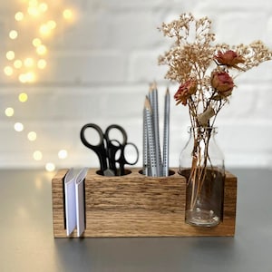Holz-Stiftehalter mit natürlicher Maserung, ausgestattet mit einer Glasvase, zwei Bohrungen für Stifte oder Scheren, einem Schlitz für Notizzettel. Kombiniert schlichtes Design mit Funktionalität – ideal für kreative und organisierte Arbeitsbereiche.